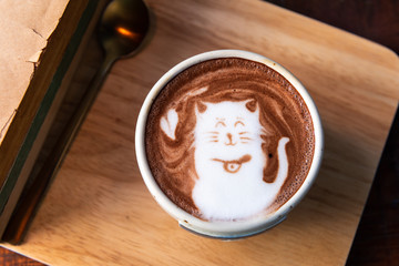 Hot cocoa cup topping cat shape with old books on wooden plate