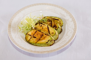 delicious fried zucchini grilled beautifully served on a platter in the restaurant,.fried zucchini in oil on a plate close-up, zucchini with toasted crust and salad on a dish