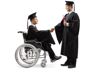 Male graduate student in a wheelchair shaking hand with a male graduate student standing and...