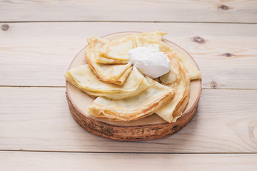 Russian thin pancakes on a wooden stand made of natural wood with sour cream . Maslenitsa is a Maslenitsa food festival.