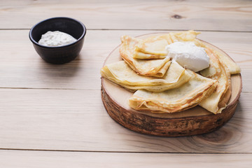 Russian thin pancakes on a wooden stand made of natural wood with sour cream . Maslenitsa is a Maslenitsa food festival.