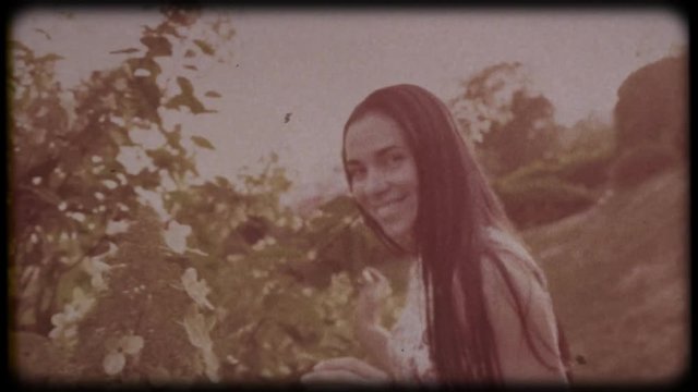 Family video archive. Retro camera 8 mm. Old film. Young attractive woman having fun in the green garden. Portrait of a smiling brunette with dimpled cheeks against a green park. Pretty girl in summer