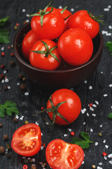 Fresh Sliced Cherry Tomatoes on a black background with spices coarse salt and herbs
