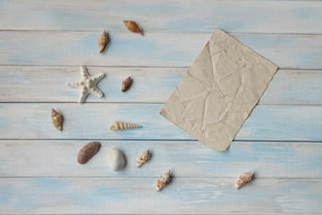 Seashells and star on blue wooden background and sheet of old paper as a vacation concept with copy space