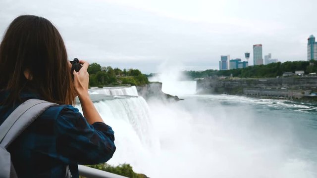 Back view of excited journalist woman with camera taking photo of epic Niagara Falls, looking around smiling slow motion