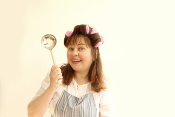 A woman posing in home clothes, in an apron, with hair curlers in her hair and playing while holding a ladle. Portrait close-up