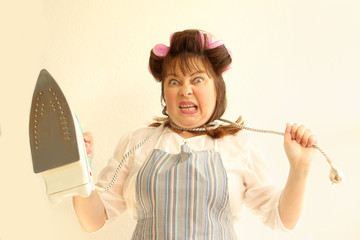A woman with an iron cord around her neck in home clothes, in an apron, with hair curlers in her...