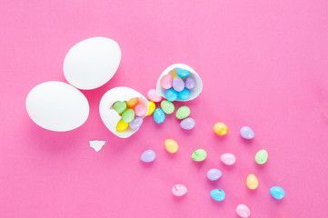 colourful easter eggs spilling out of a white egg shell on a pink background