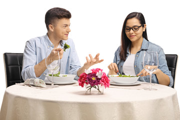 Young male and female eating a salad at a restaurant table and talking