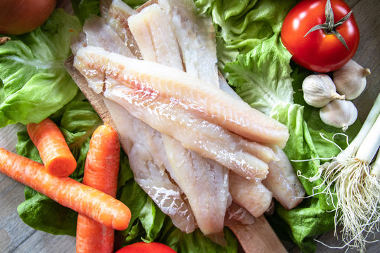 Raw hake fish fillets pieces with organic fresh vegetables in the background