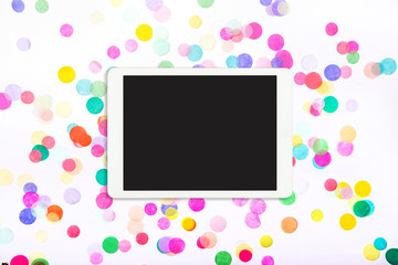 Touchpad with blank screen on colorful confetti background. Tablet computer on white background with confetti. Flat lay. Top view