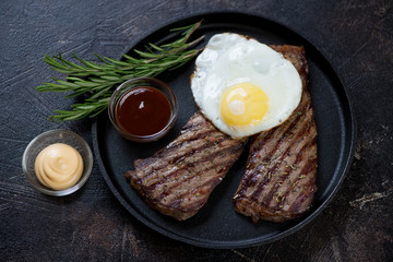 Metal serving tray with grilled beef schnitzels, fried egg and dipping sauces, studio shot