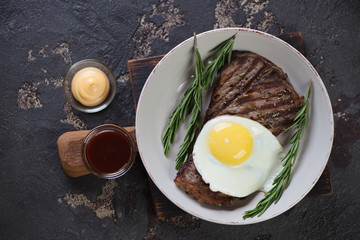 Plate with bbq beef schnitzels and fried egg, above view on a brown stone background, horizontal shot