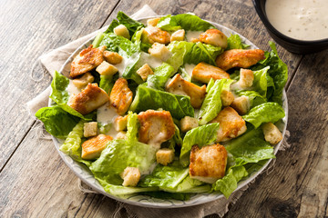 Caesar salad with lettuce,chicken and croutons on wooden table.