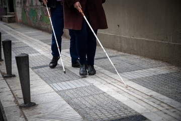 blind man and woman walking on the street using a white walking stick