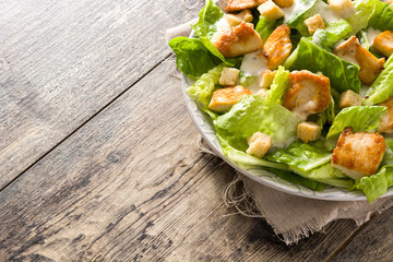 Caesar salad with lettuce,chicken and croutons on wooden table.. Copyspace