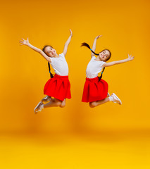 funny children girls twins jumping on colored yellow background.