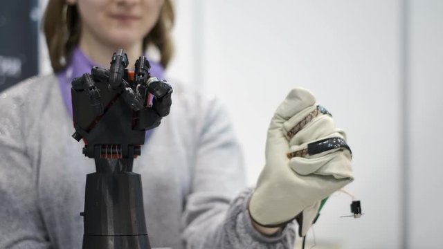 Young woman testing robotic bionic arm and making some movements. Futuristic cybernetic technology. Artificial arm mechanism. Artificial hand repeats the movements of the real hand