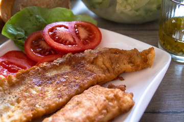 Fried hake fish fillet pieces on plate and salad