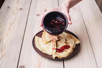 Carnival. Russian pancakes pour raspberry jam. Wooden table