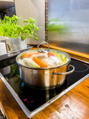 Chicken soup cooking in a pot on ceramic glas cooktop