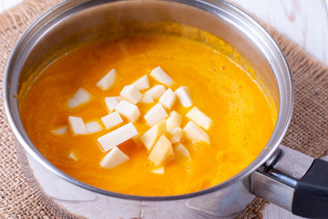 Pumpkin soup in a pan with slices of cheese on the table