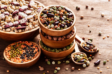 Mixed raw dried Indian legumes in wooden bowls on rustic background.
