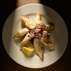 Grilled Calamari (Squid) with lemon and parsley on white plate on a plate in restaurant ready to be served