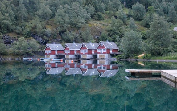 Boat houses and a dock reflecting over calm water in the famous Flam fjord, in Norway, a UNESCO site.  Photo taken past 23h (11PM), thanks to the light of the midnight Sun.