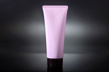 Pink cosmetic tube on a dark black background. The idea for branding or the label. Studio