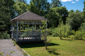 Wooden summerhouse on lawn among lush green trees on bright sunny summer day