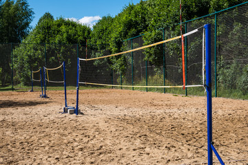 Rows of volleyball nets on blue poles on empty sand court surrounded by lush green trees on summer day