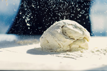 Ball of pizza dough on a rustic wooden background with dusting of flour.Making dough by female hands at bakery