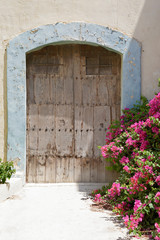 Fototapeta na wymiar Old wooden door with pink bougainvillea flowers on the right side, Malta
