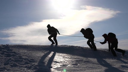 teamwork desire to win. Climbers on a rope help a friend climb to the top of the hill. Silhouette...