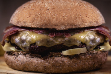 Burger with bacon, meat, tomato and lettuce on wooden background. Close up
