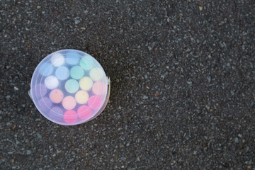 Closeup top view of closed plastic box full of new colorful chalk crayons isolated on grey sidewalk...