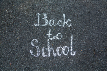 Back to school written with white chalk by kids outdoor on grey surface of pavement in city street. Horizontal color photography.