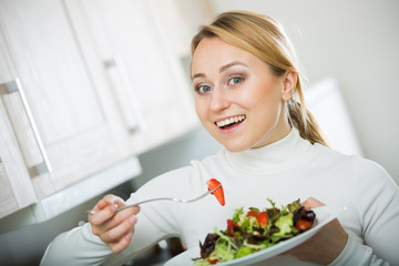 Happy girl with vegetable salad in kitchen