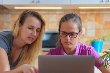 Attractive woman helping her teenage daughter to do her homework in kitchen