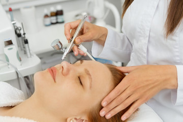 Close up of a beautiful young woman lying with her eyes closed while professional beautician performing microdermabrasion exfoliating skincare cosmetology cosmetologist facial beauty peeling