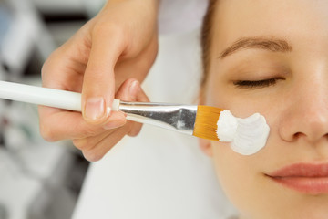 Naklejka premium Cropped close up of a beautician applying facial mask on a young female face client service treatment therapy therapist dermatology cosmetology refreshing pampering wellness spa recreation skincare