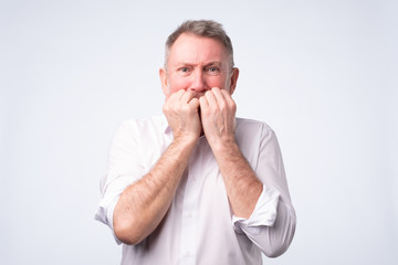 Senior man in white shirt biting nails in fear