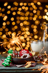 Gingerbread mittens, little man, snowflakes, christmas trees in a brown wooden plate and a bottle of milk on a green wooden on the background of blurred garland. close up. space