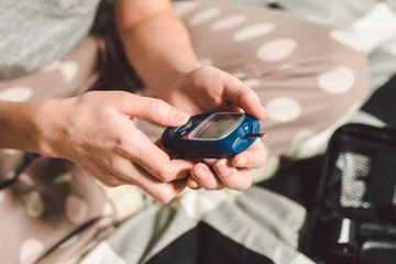 Theme diabetes. A close-up macro plan. Hands of a young Caucasian woman at home in the bedroom on the bed. It uses the technology of an instrument for measuring the level of glucose in the blood