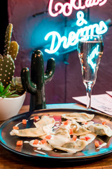Beautiful dumplings with sour cream on a black plate on the background of a neon sign in a restaurant. close-up