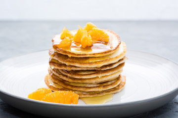 Delicious homemade pancakes with tangerines and honey on a plate on the table. Close-up