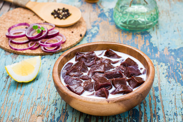 Pieces of raw beef liver soaked in milk in a wooden bowl and ingredients for cooking on the table