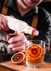 Bartender does beautiful cocktail with Sicilian orange in a transparent glass on the bar.space. close up