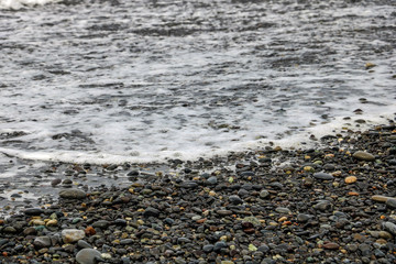 Pebbles on a sandy beach, shiny wet stones and waves.